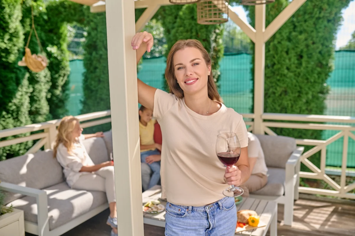 Woman enjoying wine in a custom garden structure design featuring comfortable seating and decorative elements.