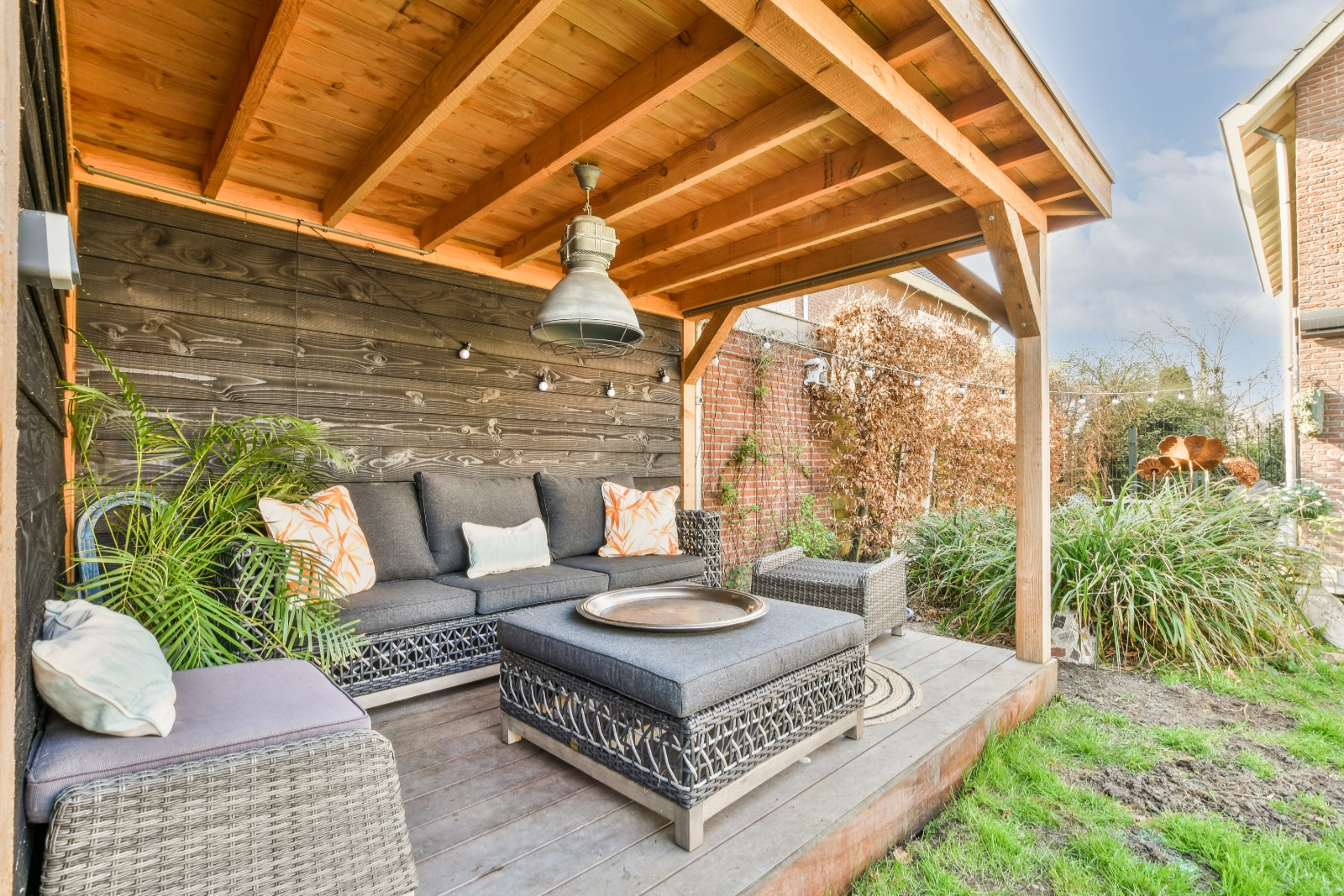 Cozy outdoor seating area under a wooden garden structure with modern furniture and natural surroundings.