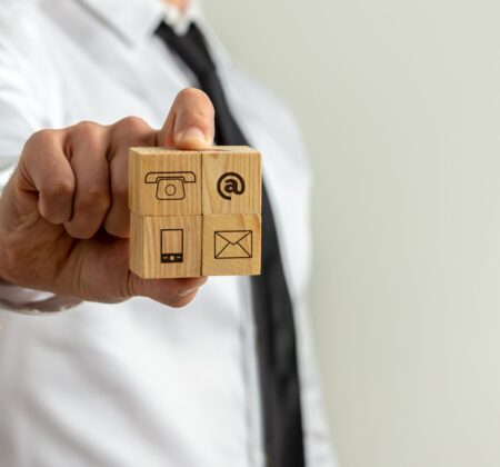 Businessman showing four wooden cubes with contact and communication icons toward the camera.