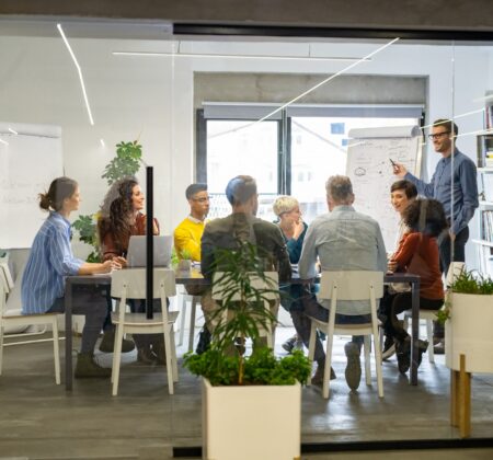 Confident mature businessman giving a presentation to his crative team in office. Business brief with annual goals with casual employees. Happy leadership man training young businessmen and smiling businesswomen sitting at conference table.